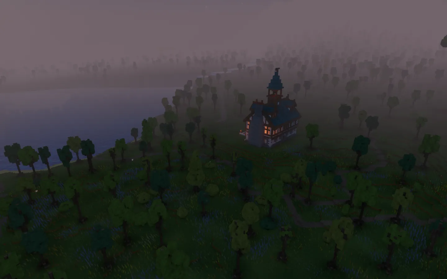 A timber town hall with a blue-green roof and lit windows beside the lake at dusk, surrounded by dark meadow and trees.