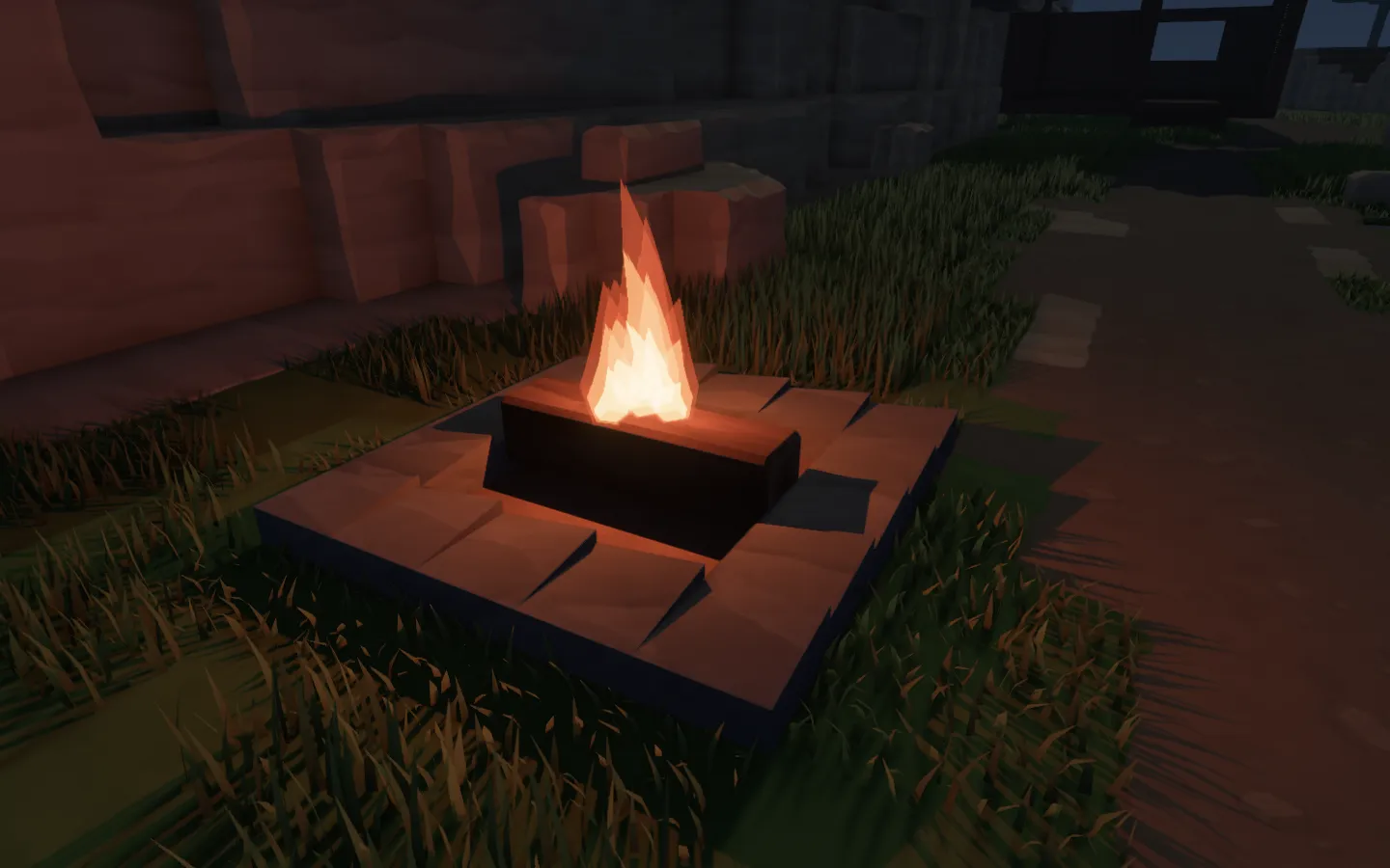 A small fire burning in a stone hearth at night, lighting the surrounding grass and sandstone in orange.