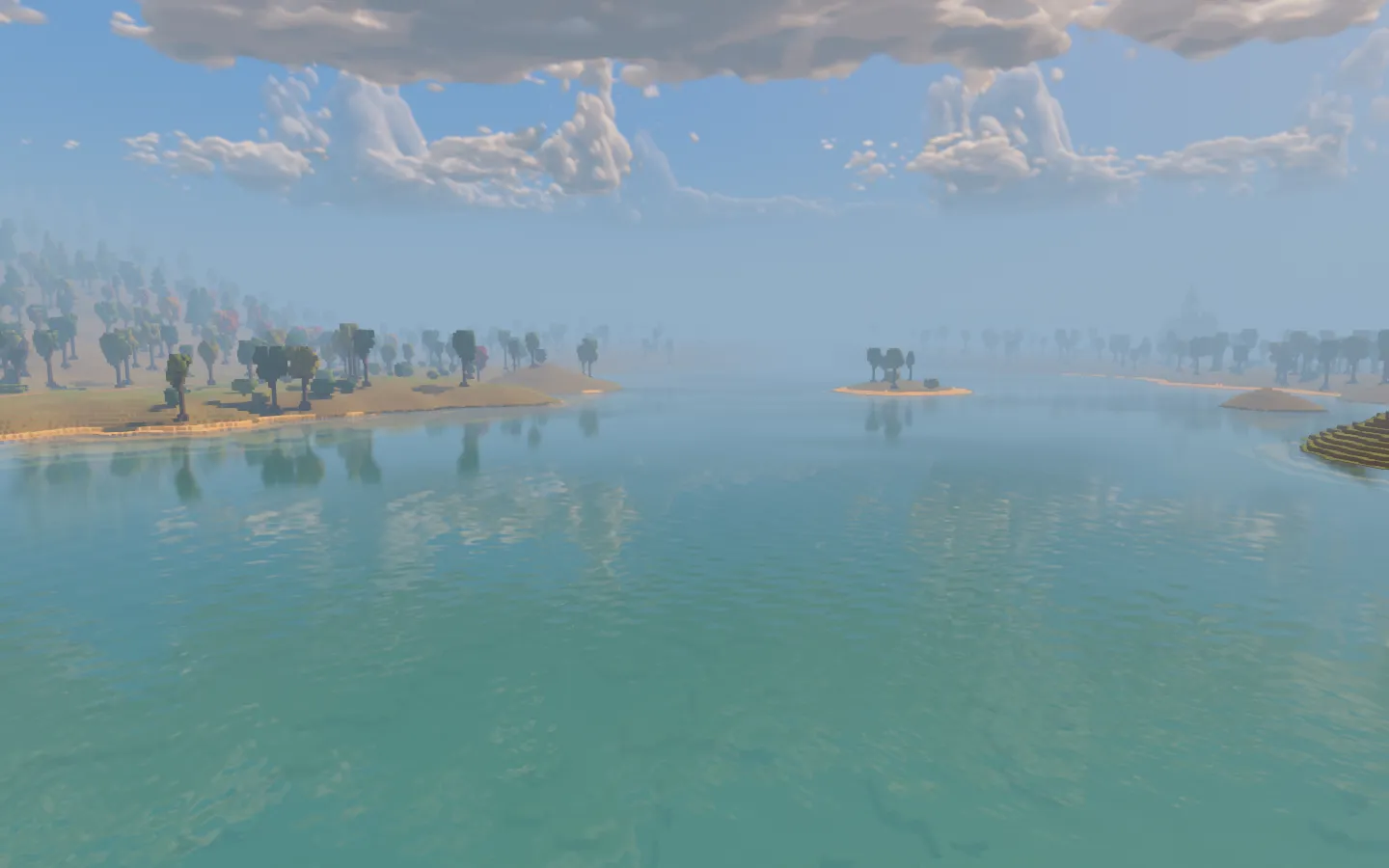 The calm turquoise valley lake with sandy islands and wooded shores reflected in its surface beneath a clouded sky.