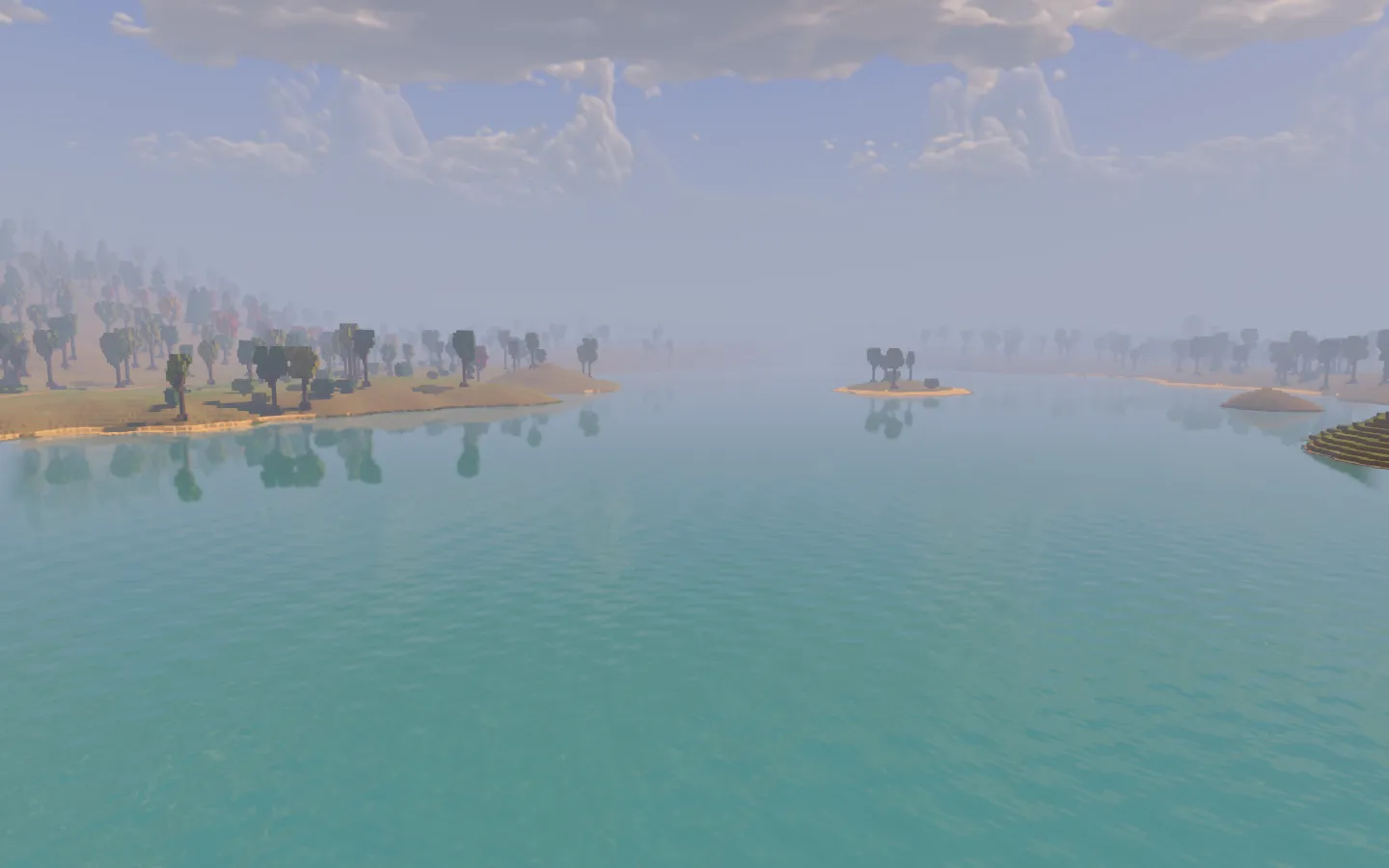 A broad turquoise lake with sandy islands and wooded shores fading into the distance beneath pale clouds.